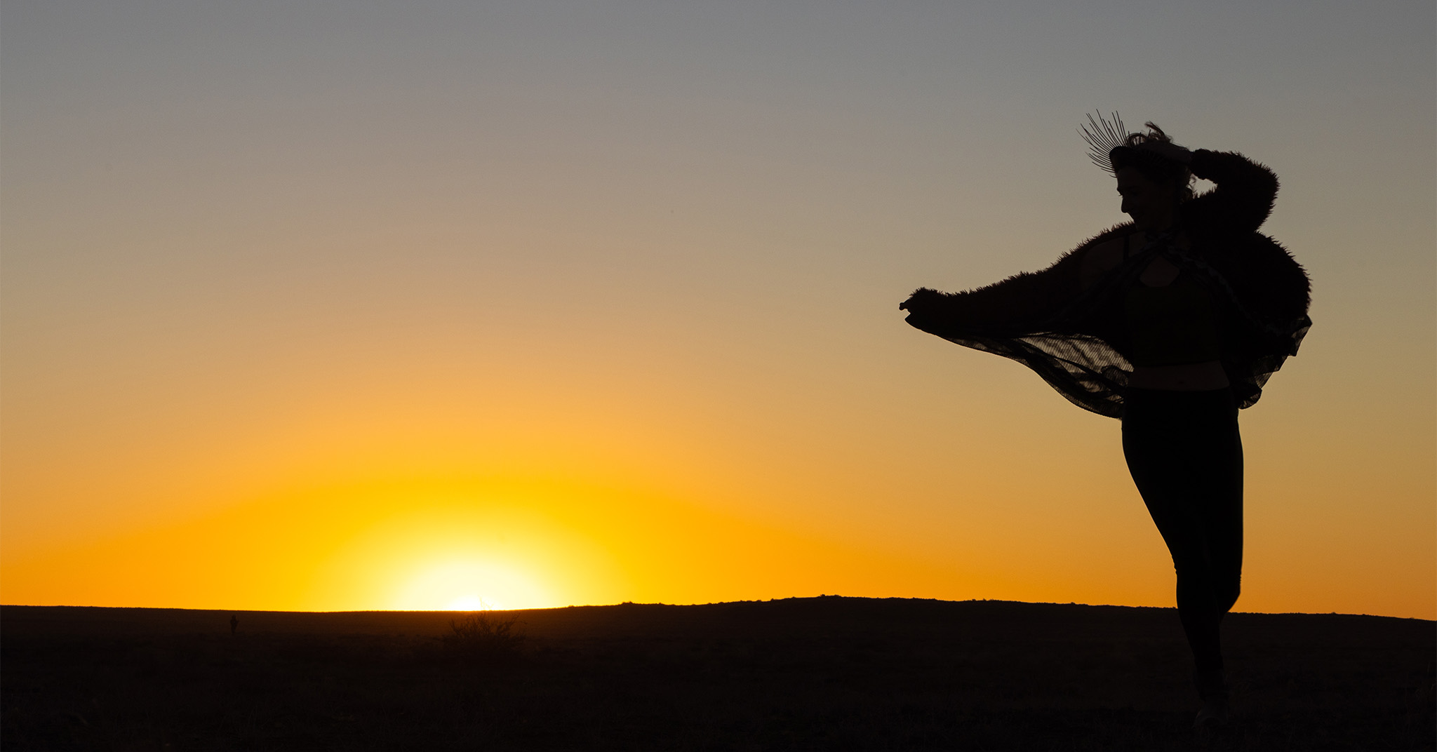 A dancing woman silhouetted by a desert sunset.
