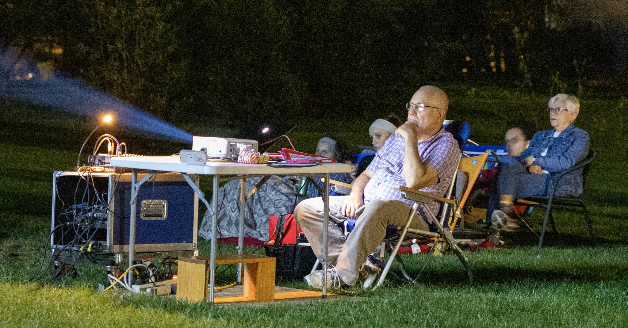 A man looking out of frame. He is watching a movie being projected by a projector on a table.
