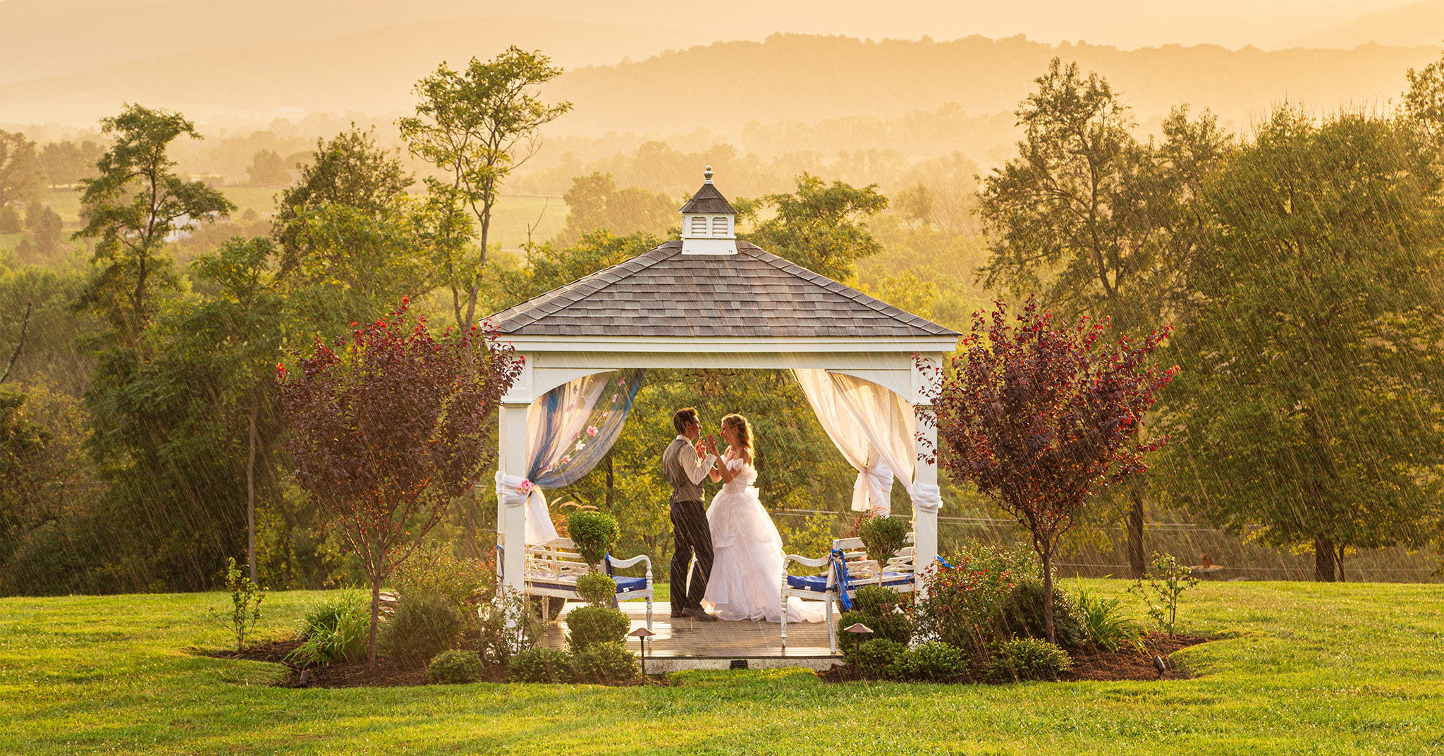 A smiling wedding couple standing in a gazebo at sunset. It is raining lightly.